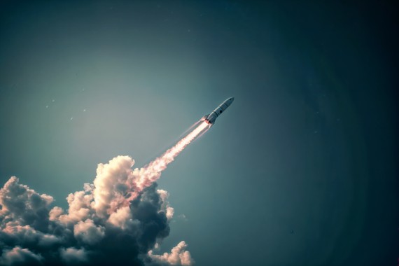 Photo of an starship rocket flying in the sky, leaving behind it pink smoke and leaving its trail on top of the background. The scene is captured from below with high resolution, showcasing details of both the rocket's body and its streaks against the greyish blue backdrop of open skies. This shot highlights the sleek design of space equipment against the vast expanse of nature, creating a sense of awe as if looking at the flight moment itself. --ar 3:2 --style raw